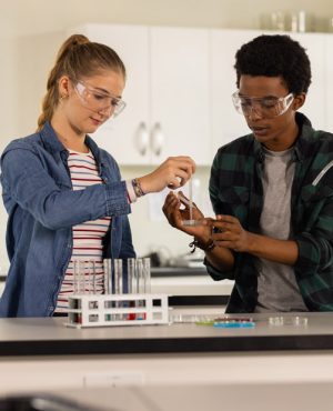 In high school laboratory, teenagers conducting science experiment with beakers and test tubes. Education, students, chemistry, teamwork, STEM, learning