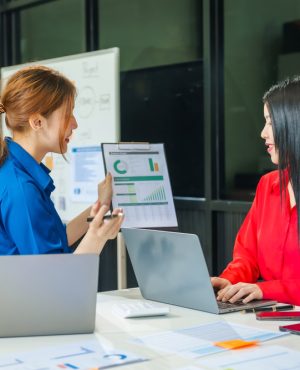 Two young female business consultants work on startup, collaborating on mobile app development social media strategies. whiteboards, documents, they aim to build a successful e-commerce business.